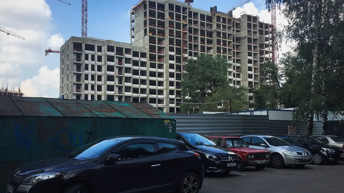 Строящийся многоэтажный жилой дом и автомобили во дворе