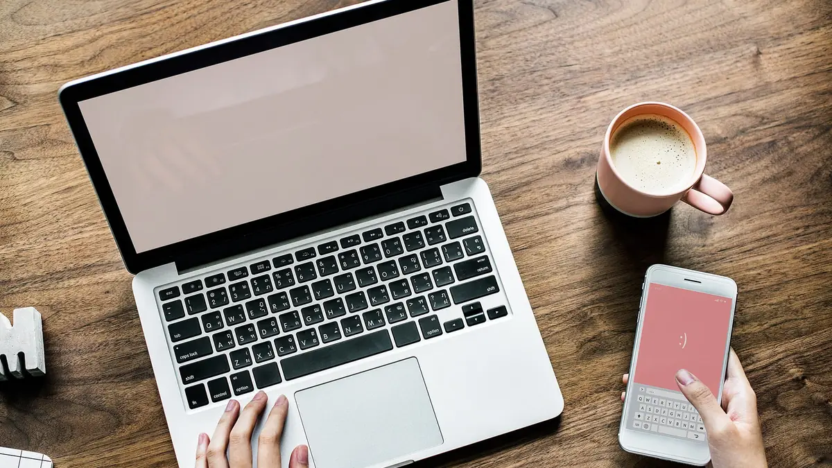 Руки на ноутбуке и смартфоне на деревянном столе, вид сверху